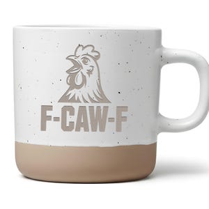 Könnte beinhalten: Eine weiße Keramiktasse mit beigem Boden und Henkel. Die Tasse zeigt eine stilisierte Hahn-Grafik über dem Text "F-CAW-F". Die Tasse hat eine gesprenkelte Oberfläche.