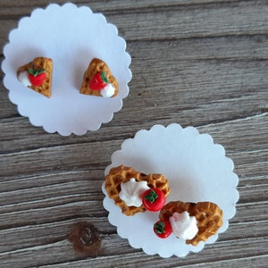 Puede incluir: Pendientes de gofres en forma de coraz&oacute;n con fresas y crema batida, presentados sobre tarjetas blancas festoneadas. Los pendientes son de color marr&oacute;n dorado y descansan sobre una superficie de madera. Cada pendiente es un gofre en miniatura.