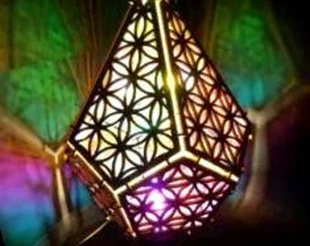 May include: A geometric, pyramid-shaped lamp with a floral pattern cut into its sides. The lamp emits a colorful glow, with shades of purple, green, and yellow. The lamp is made of a dark material and has a modern design.