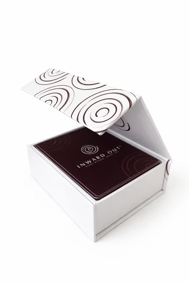 Peut inclure: Une bo&icirc;te blanche avec un couvercle &agrave; charni&egrave;re contenant un jeu de cartes. Le couvercle et le dessus des cartes pr&eacute;sentent un motif en spirale marron. Les cartes sont marron fonc&eacute; avec le texte "INWARD OUT" et un logo en spirale.