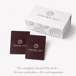Puede incluir: Una caja blanca y dos tarjetas de color rojo oscuro con el texto "INWARD OUT" y un diseño en espiral. La caja tiene el mismo texto y diseño. El texto en la parte inferior dice "La baraja completa Inward Out - 56 cartas principales más una expansión de 28 cartas."