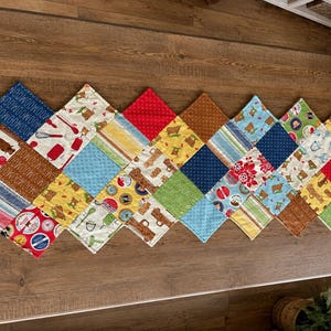 May include: A rectangular quilted table runner composed of numerous diamond-shaped fabric patches in a variety of colors and patterns, including red, blue, yellow, green, and brown, featuring prints of kitchen utensils, trucks, and geometric motifs.
