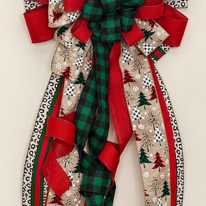 May include: A decorative bow featuring multiple ribbons in solid red, green and black plaid, and a tan burlap-style fabric printed with red, green, and black-and-white buffalo check Christmas trees, snowflakes, and leopard print patterns.