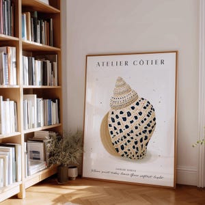 Può includere: Una stampa artistica verticale incorniciata con un'illustrazione dettagliata di una conchiglia color marrone chiaro con motivi a macchie blu scuro. Il testo ATELIER CÔTIER, LUMIERE MARINE e Where quiet tides leave their softest light è stampato in nero.