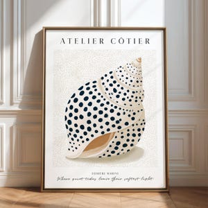 Puede incluir: Una lámina enmarcada que muestra una concha de color crema con lunares azul marino oscuro. El texto ATELIER CÔTIER aparece en la parte superior, con LUMIÈRE MARINE y la frase Where quiet tides leave their softest light en la parte inferior.