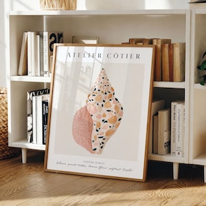 May include: A framed rectangular wall art print featuring a large, stylised seashell illustration in shades of pink, orange, and dark blue. The text ATELIER CÔTIER and LUMIÈRE MARINE with the phrase Where quiet tides leave their softest light appear.