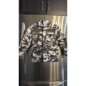 May include: A white ceramic mug with a black handle and the text "But First, Coffee" in a bold, black font. The mug is filled with a dark liquid, likely coffee, and sits on a light-colored surface.