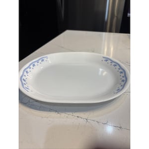 May include: An oval white serving platter featuring a delicate blue floral pattern along the rim. The dish has a smooth, glossy finish and a simple, clean design, providing a classic look for serving food at any dining table or gathering.