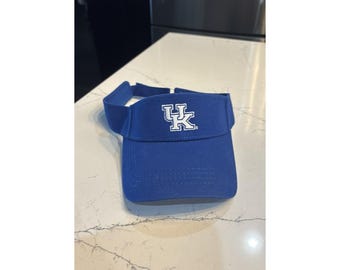 May include: A royal blue visor with a curved brim and a band. The visor features a white logo in the center. The visor is made of a soft, durable material.