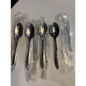 May include: Four stainless steel spoons, each individually wrapped in clear plastic. The spoons have a classic teardrop bowl shape and a long, slender handle. The spoons are arranged in a row, ready for use.
