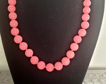 May include: A single-strand necklace composed of smooth, round, opaque pink beads of uniform size. The necklace is displayed on a black bust. A small white rectangular tag at the base features the black printed text N-PK 17.