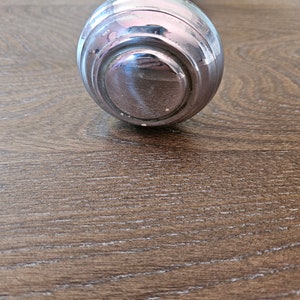 May include: A silver door knob with a round, smooth design. The knob is on a wooden surface.