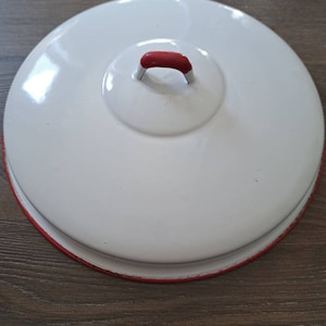 May include: White enamelware lid with a red rim and a red handle. The lid is round and has a smooth surface.