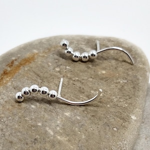 May include: A pair of silver earrings with a curved shape and a row of small silver beads.