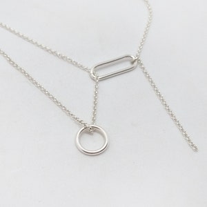 Könnte beinhalten: Eine silberne Halskette mit einer zarten Kette und zwei Anhänger: ein kleiner Kreis und ein größeres Oval.