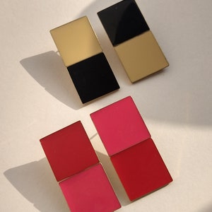 Op de afbeelding: Twee paar geometrische oorbellen. Het ene paar is zwart en goud, het andere is rood en roze.
