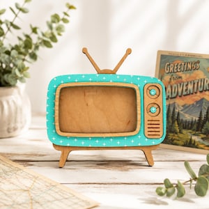 May include: A wooden television-shaped picture frame featuring a bright teal front panel with a white star pattern. The frame includes two top antennas, a rectangular screen opening, two circular knobs, and a speaker grille on the right side.