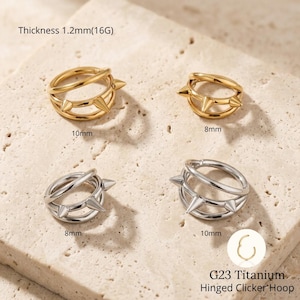 Puede incluir: Cuatro aros articulados en oro y plata. Los aros dorados tienen 10 mm y 8 mm de diámetro, y los aros plateados tienen 8 mm y 10 mm. Cada aro presenta un diseño de púas. El texto dice: Grosor 1,2 mm (16G) y G23 Titanium Hinged Clicker Hoop.