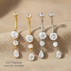 May include: Four belly button rings with clear, sparkling gemstones. Two are gold-toned, and two are silver-toned. Each ring features a curved barbell with a large, round gem, two smaller gems, and a teardrop-shaped gem. The text "G23 Titanium Internally threaded" is visible.