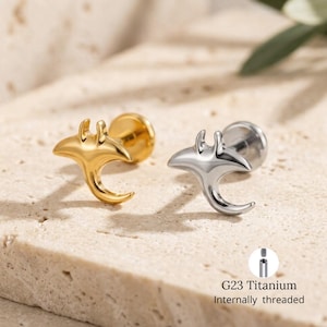 Op de afbeelding: Twee oorknopjes met een manta ray-ontwerp. Eén is goudkleurig, de andere zilverkleurig. De oorbellen zijn gemaakt van G23 titanium en zijn intern schroefdraad.