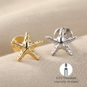 May include: Two starfish earrings, one gold and one silver, are shown on a neutral fabric. The earrings have a textured surface and are designed with a post and backing. The image also includes a close-up of the earring post with the text "G23 Titanium Internally threaded."