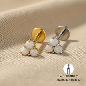 Może przedstawiać: Dwie kolczyki z trzema białymi kamieniami opalu w trójkącie. Jeden jest złoty, drugi srebrny. Obraz zawiera schemat wewnętrznego gwintowanego słupka tytanowego G23.