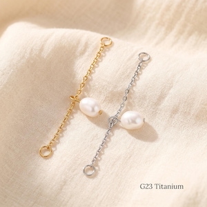 May include: Two jewelry chain connectors made of G23 titanium, one in a gold tone and one in a silver tone. Each chain features a single white oval-shaped pearl charm attached to the center, with a small circular jump ring at each end of the chain.