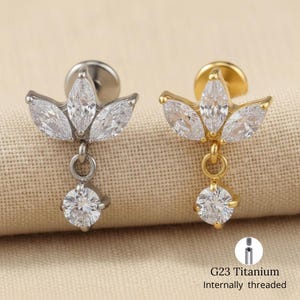 Può includere: Due orecchini in titanio G23 con filettatura interna. Uno è argentato, l'altro dorato. Ognuno presenta un design a cristallo a forma di marquise con un cristallo rotondo pendente. Gli orecchini sono progettati per piercing.