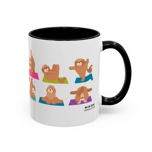 May include: White ceramic mug with a black interior and handle. The mug features illustrations of a brown dog in various yoga poses on colorful mats. The text "Blue Dog Lifestyle & Gifts" is printed on the side.