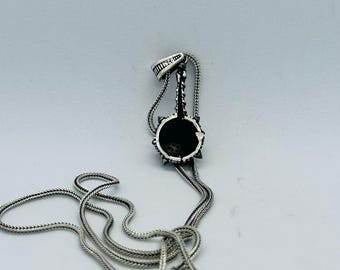 May include: A silver-toned pendant necklace featuring a circular pendant with a spiky border and a detailed design. The necklace has a delicate chain and a lobster clasp. The pendant is approximately 1 inch in diameter.