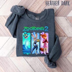 Puede incluir: Sudadera gris oscuro jaspeado con el texto "Zootopia 2" e ilustraciones de personajes. El dise&ntilde;o incluye una serpiente azul, Judy Hopps y Nick Wilde. La sudadera es de un material suave.