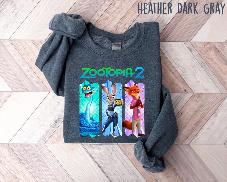 Puede incluir: Sudadera gris oscuro jaspeado con el texto "Zootopia 2" e ilustraciones de personajes. El dise&ntilde;o incluye una serpiente azul, Judy Hopps y Nick Wilde. La sudadera es de un material suave.