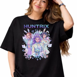 May include: Black t-shirt with the word "HUNTRIX" in a gradient colour scheme above a graphic of three anime-style characters wearing bunny ears. The graphic includes floral and geometric elements.