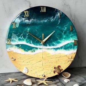 Puede incluir: Reloj de pared redondo con diseño de escena de playa. La esfera del reloj presenta una playa arenosa, olas del océano y números romanos dorados. Estrellas de mar, conchas marinas y una tortuga decorativas están dispersas en la esfera.