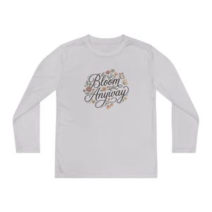 May include: A light gray long-sleeve shirt featuring a central graphic with the text "Bloom Anyway" in a black cursive script, surrounded by small illustrations of orange and pink flowers, green leaves, and two small butterflies.
