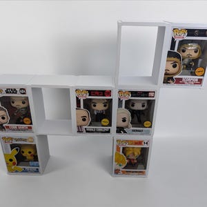 Op de afbeelding: Een witte, geometrische display-plankeenheid met verschillende Funko Pop!-figuren in hun originele dozen. De figuren bevatten personages uit Star Wars, The Witcher en andere popcultuurfranchises. De plank is ontworpen om verzamelobjecten te presenteren.