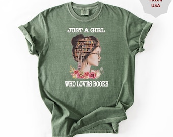 May include: Green t-shirt with the text "JUST A GIRL WHO LOVES BOOKS". The graphic features a woman's profile with a bookshelf in place of her hair, surrounded by flowers. The shirt is a solid green color.