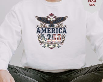 May include: White sweatshirt featuring a patriotic design. The graphic includes an eagle with outstretched wings, the word "AMERICA", the number "250", the Statue of Liberty, and the text "EST. 1776".
