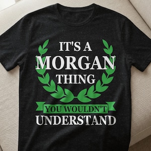 Könnte beinhalten: Schwarzes T-Shirt mit dem weißen und grünen Text "IT'S A MORGAN THING YOU WOULDN'T UNDERSTAND". Der Text ist in einem kreisförmigen Design mit grünen Blättern angeordnet. Das Shirt ist aus weichem Material.