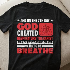 Könnte beinhalten: Schwarzes T-Shirt mit weißem und rotem Text. Der Text lautet: „UND AM 7. TAG SCHUF GOTT ATEMTHERAPEUTEN, WEIL ALLES, WAS ER ERSCHUF, ATMEN MUSS.“ Ein rotes Rechteck enthält eine Lungengrafik.