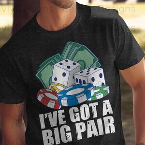May include: Dark grey t-shirt featuring a poker-themed design with dice, casino chips, and banknotes. The text "I'VE GOT A BIG PAIR" is printed in white.