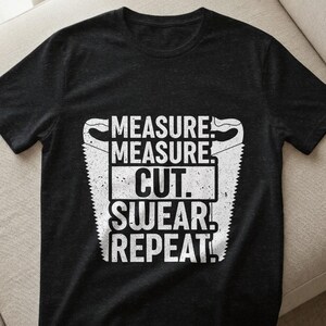 Könnte beinhalten: Dunkelgraues T-Shirt mit weißem Aufdruck. Der Aufdruck zeigt den Text "MEASURE. MEASURE. CUT. SWEAR! REPEAT!" in einer kräftigen, verwitterten Schriftart, mit Sägeblatt-Illustrationen auf beiden Seiten.