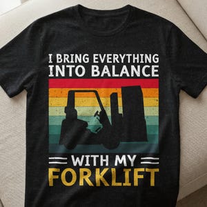 May include: Black t-shirt with the text "I Bring Everything Into Balance With My Forklift." The design features a forklift silhouette against a retro striped background in red, orange, yellow, and green.
