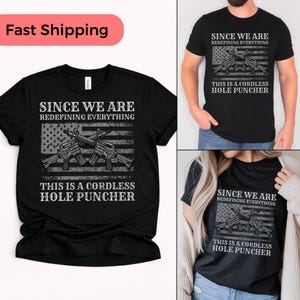 Può includere: T-shirt nero con la scritta "SINCE WE ARE REDEFINING EVERYTHING" sopra un disegno della bandiera americana e due fucili. Sotto c'è la scritta "THIS IS A CORDLESS HOLE PUNCHER".