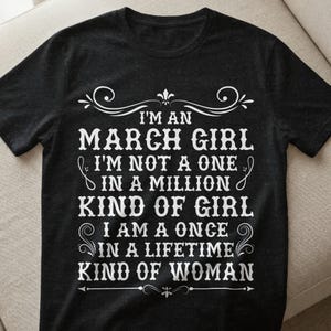 Könnte beinhalten: Dunkelgraues T-Shirt mit weißem Text: "I'M AN MARCH GIRL I'M NOT A ONE IN A MILLION KIND OF GIRL I AM A ONCE IN A LIFETIME KIND OF WOMAN". Rundhalsausschnitt.