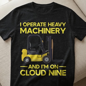 May include: Dark grey t-shirt featuring a yellow forklift graphic and the text "I OPERATE HEAVY MACHINERY". Below the forklift, the text reads "AND I'M ON - CLOUD NINE". The shirt is made of a soft material.
