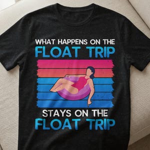 Könnte beinhalten: Schwarzes T-Shirt mit dem Text "WHAT HAPPENS ON THE FLOAT TRIP STAYS ON THE FLOAT TRIP". Das Design zeigt eine Person in einem rosa Badeanzug, die sich auf einem Schwimmreifen vor einem farbenfrohen gestreiften Hintergrund entspannt.