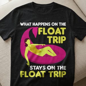 May include: Dark grey t-shirt featuring the text "WHAT HAPPENS ON THE FLOAT TRIP STAYS ON THE FLOAT TRIP". The design includes a person in a yellow swimsuit on a pink float. The t-shirt is made of a soft fabric.