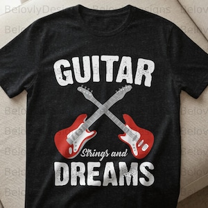 May include: Dark gray t-shirt with the word "GUITAR" in large white letters above two crossed red and silver electric guitars. Below the guitars, the text reads "Strings and DREAMS" in white.