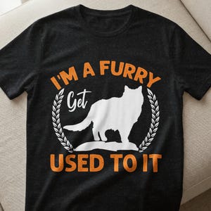 Könnte beinhalten: Dunkelgraues T-Shirt mit dem Text "I'M A FURRY GET USED TO IT" in Orange und Weiß. Eine weiße Wolfssilhouette ist in einem Lorbeerkranz zentriert.